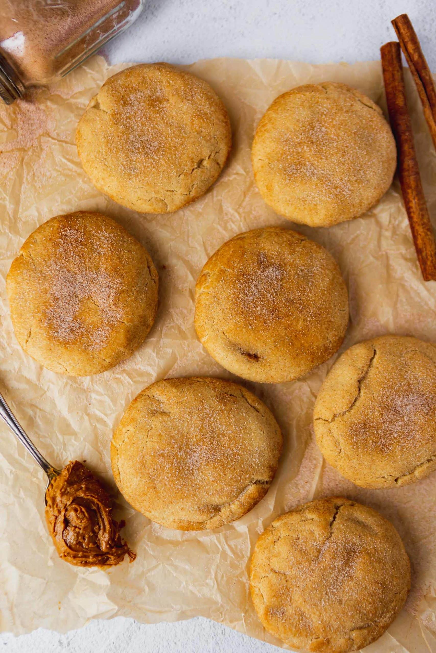 Baked large and thick snickerdoodles on parchment paper. They are sprinkled with cinnamon sugar and a spoonful of biscoff is next to the cookies.