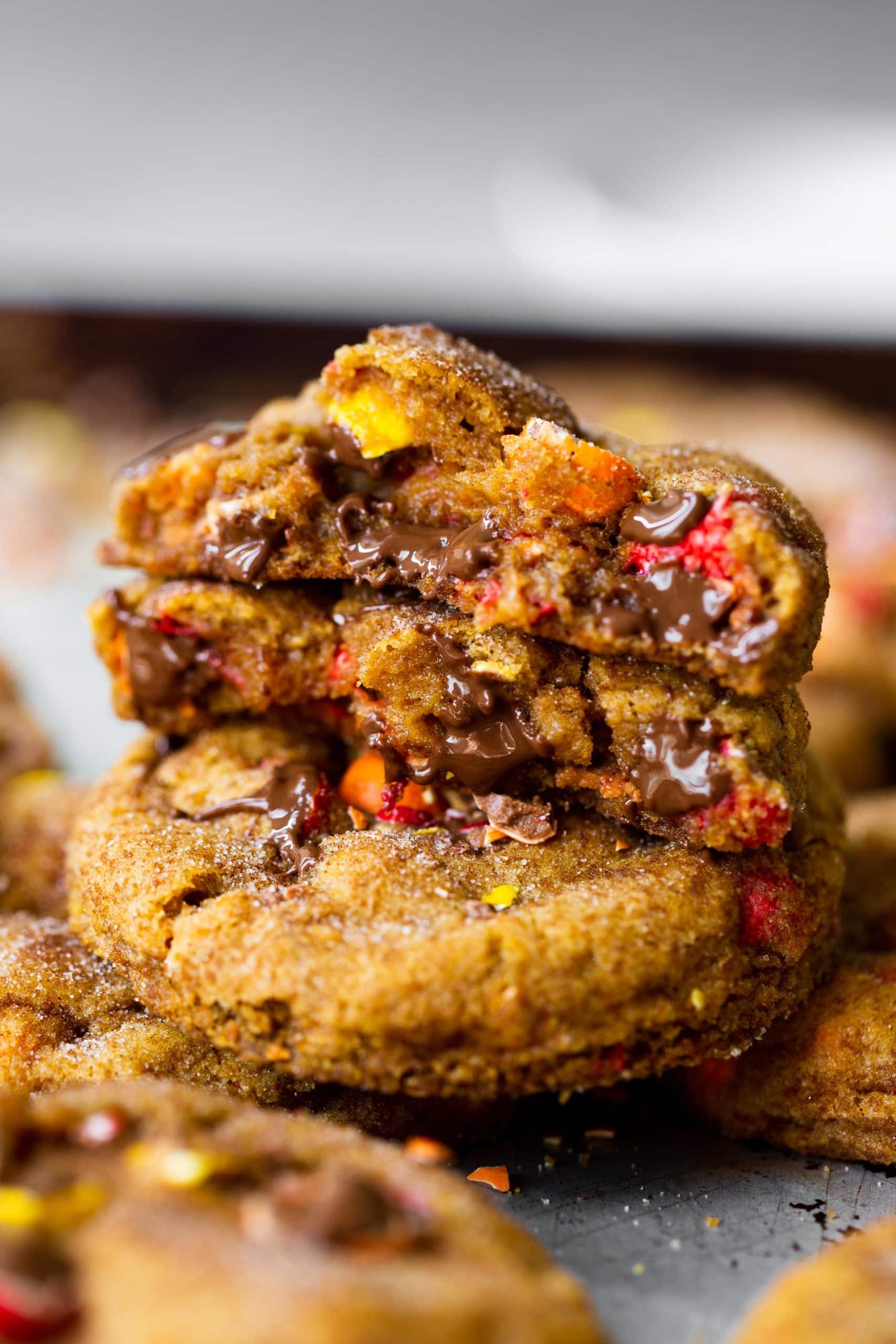 a photo of a stack of chewy pumpkin cookies filled with cadbury chocolate bits. the top cookie is broken in half with the inside of the cookies showing.