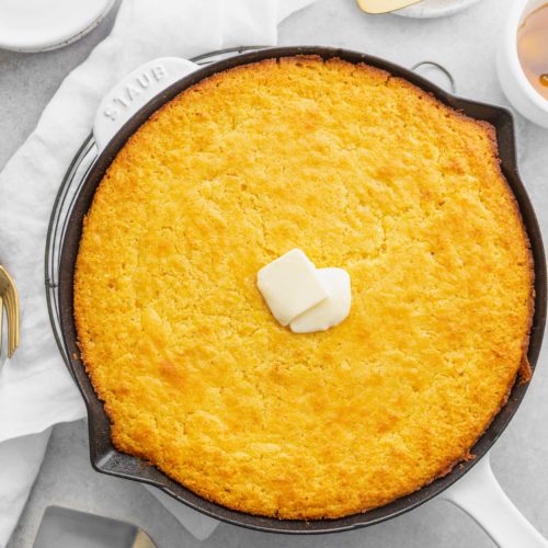 A cast iron skillet with baked cornbread. Two little cubes of butter are in the center of the cornbread.