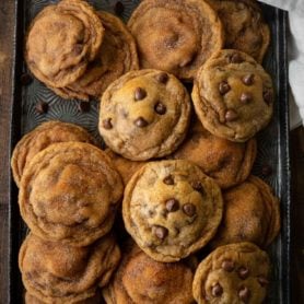a photo of a cookie sheet full of baked pumpkin pudding cookies. some have chocolate chips and some are covered with cinnamon and sugar.