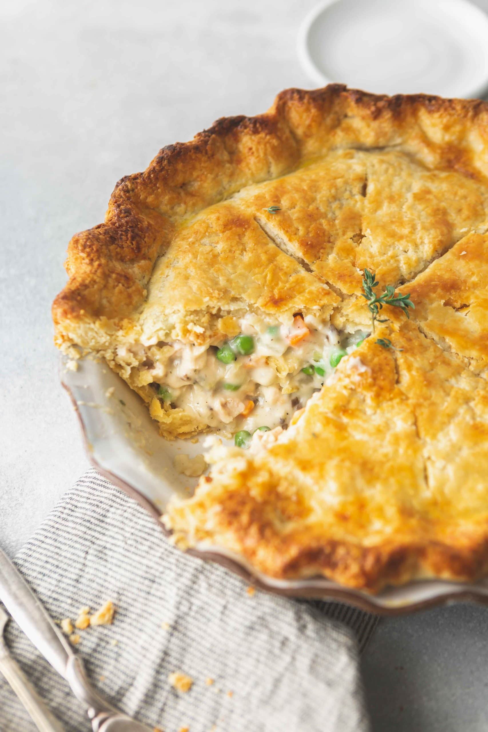A baked turkey pot pie that has a slice removed showing the creamy filling with turkey, peas and carrots.