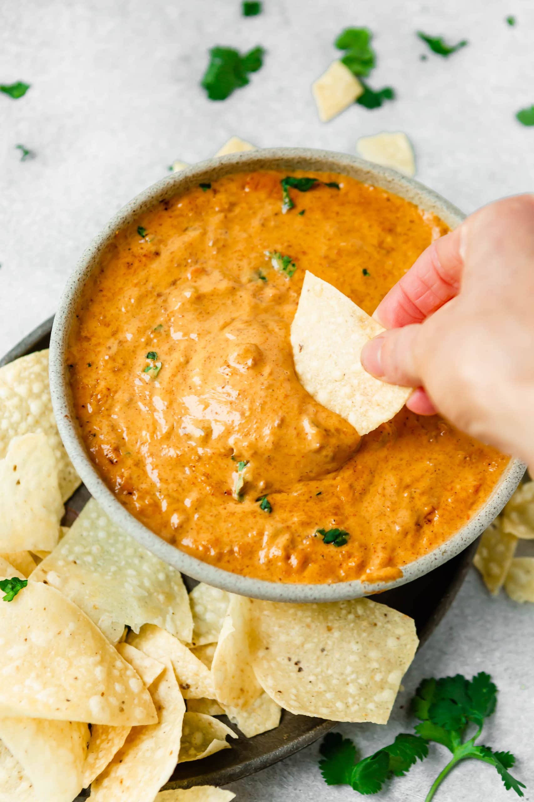 A bowl of chilis queso dip. A tortilla chip is being dipped into the cheese. and more chips are around the bowl of dip.