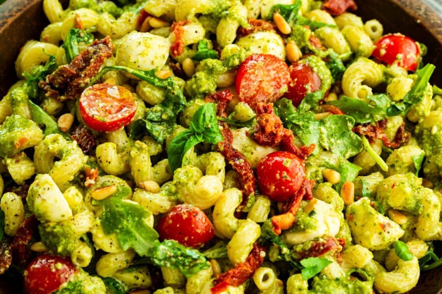 a large bowl of creamy pesto pasta with halved cherry tomatoes, arugula and sun dried tomatoes