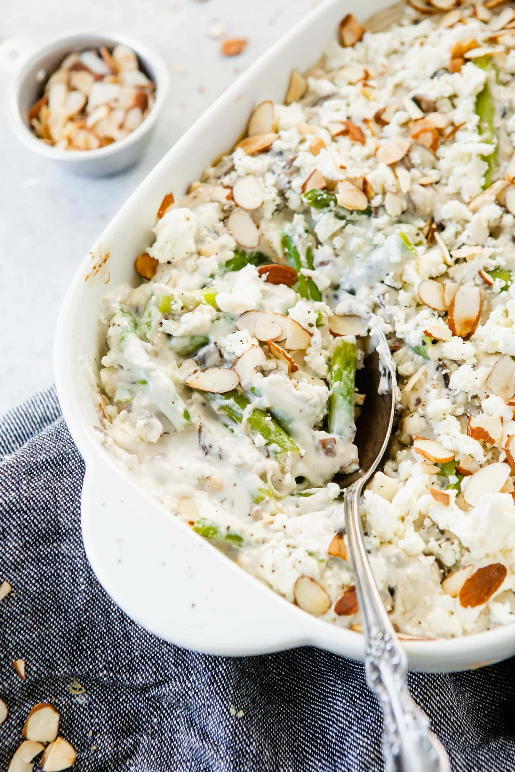 A close up picture of green beans with feta. A serving spoon is in the dish. You can see the creamy white sauce and the green bean that are topped with sliced almonds.
