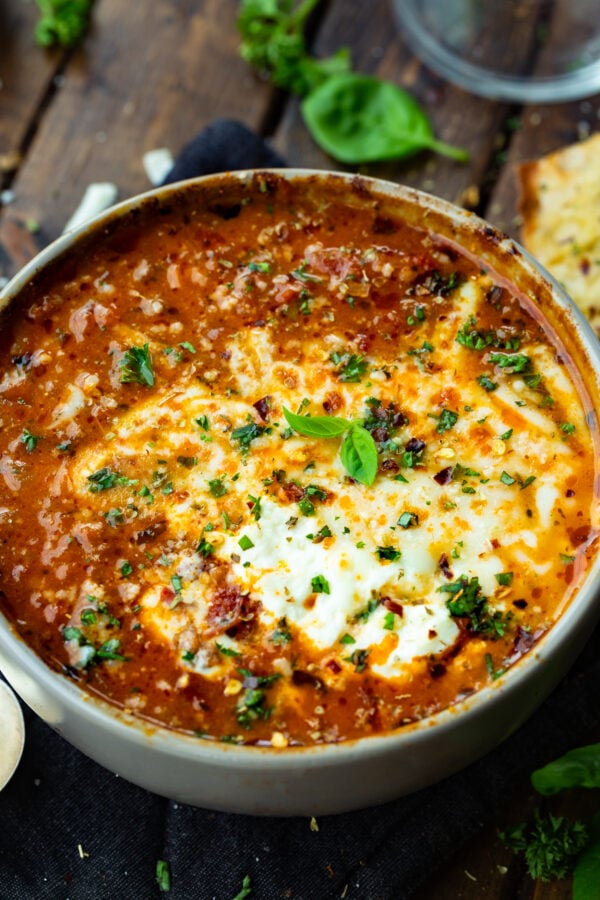 a photo of a large bowl of hearty italian style beef chili topped with melted cheese, sour cream and chopped fresh herbs.