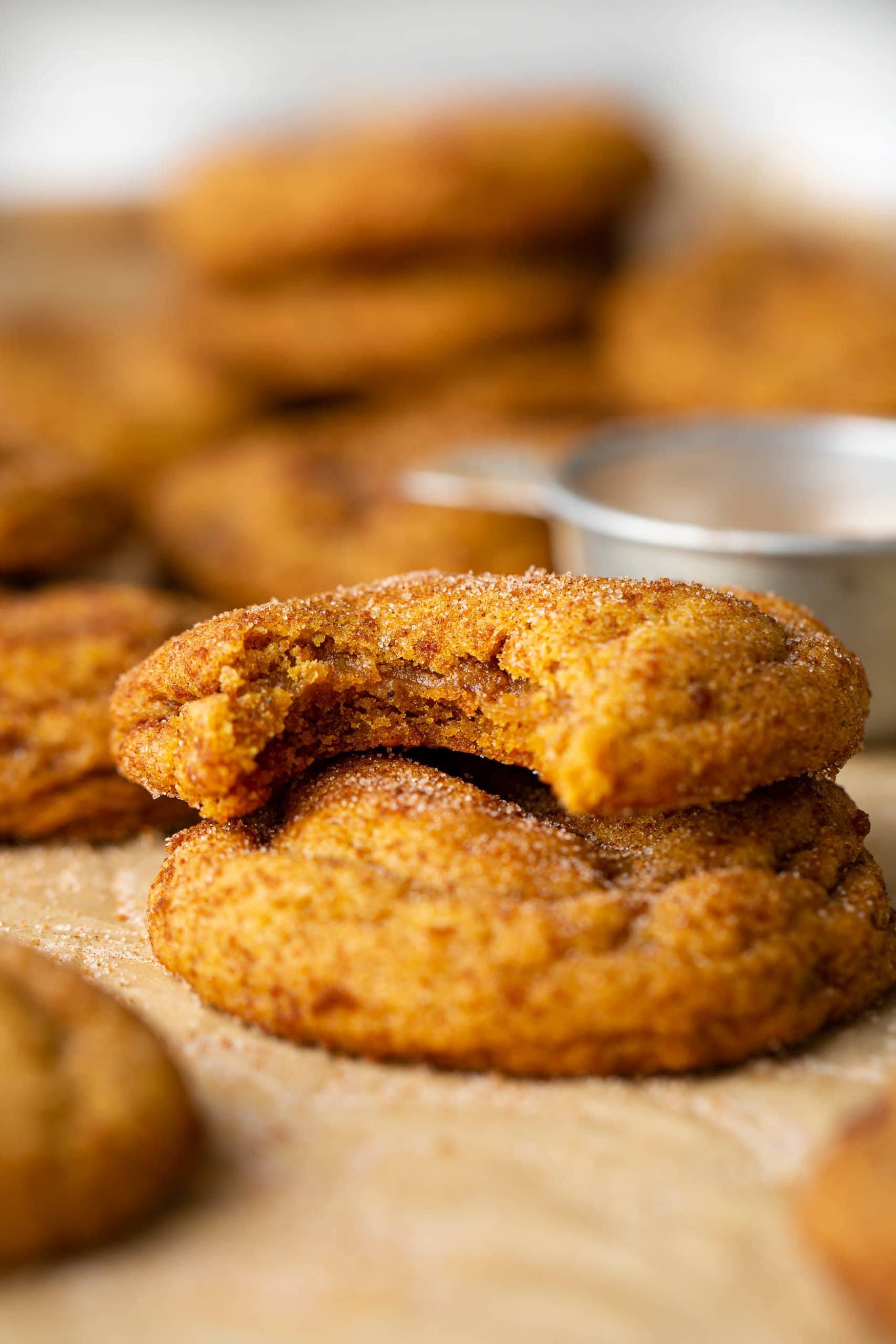Two chewy pumpkin cookies stacked on top of each other. The top on has a bite taken out of it. They are topped with brown sugar and cinnamon.