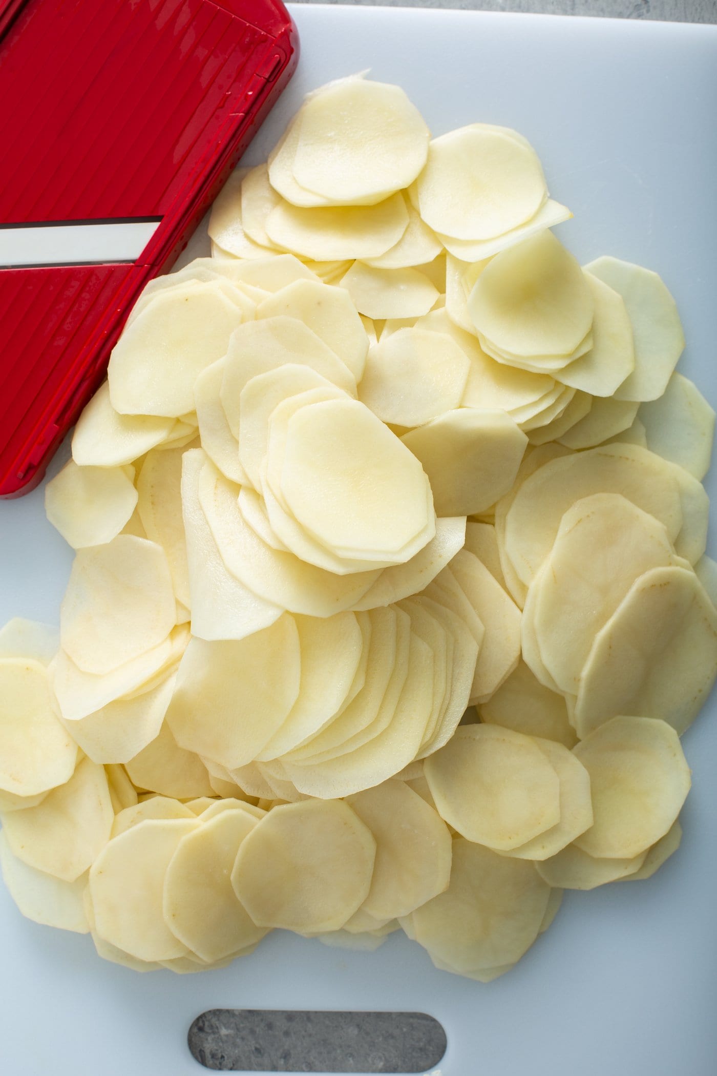 Raw, peeled, sliced potatoes with a red and white kitchen towel in the background.