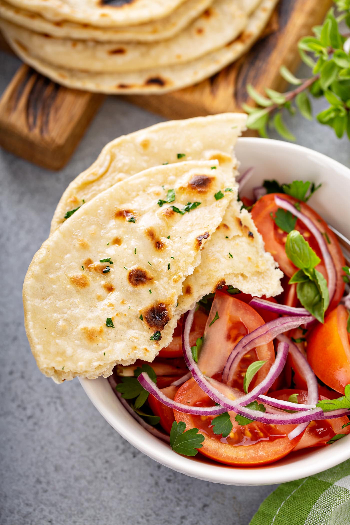 A photo of a bowl of fresh tomato and onion salad in a white bowl with torn pieces of unleavened bread sitting on the side of the bowl.