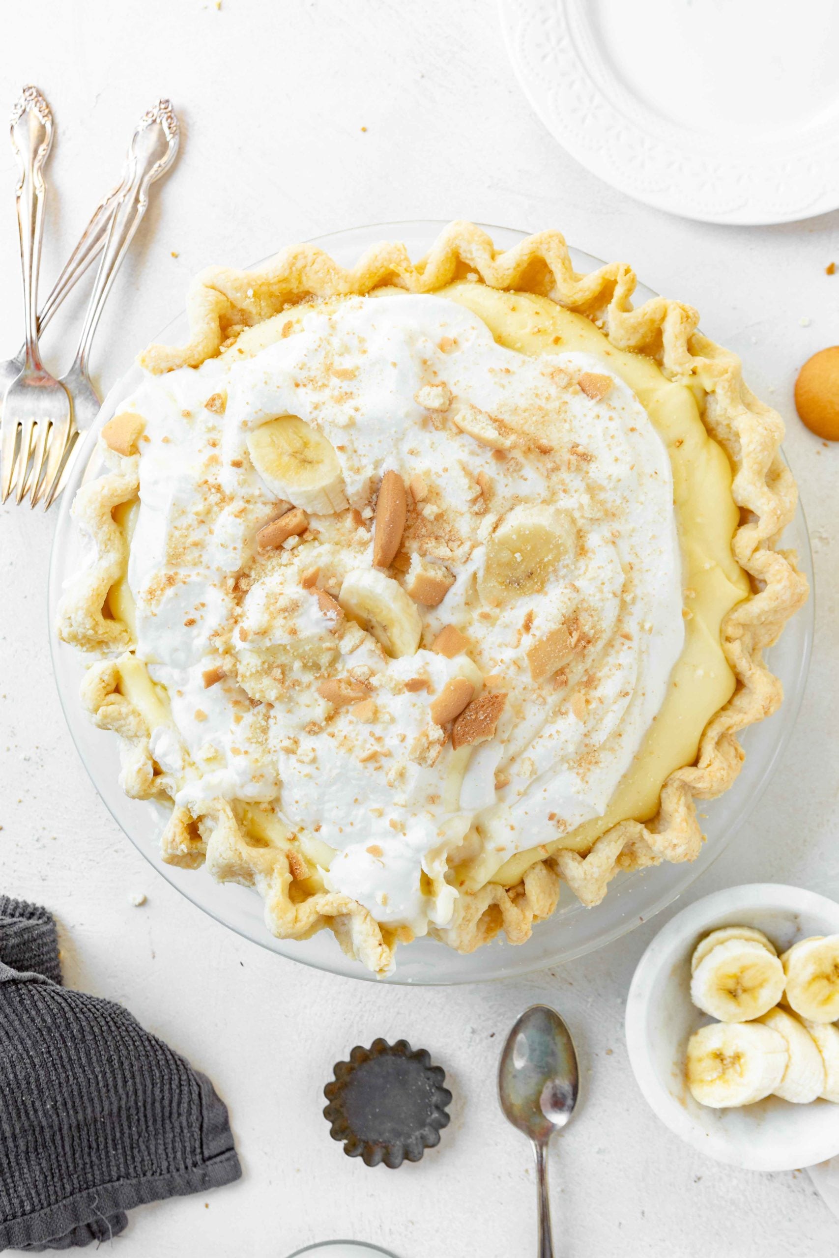a photo of a whole banana cream pie in a homemade pie crust. the pie is topped with whipped cream, fresh banana slices, and crushed Nilla Wafers.