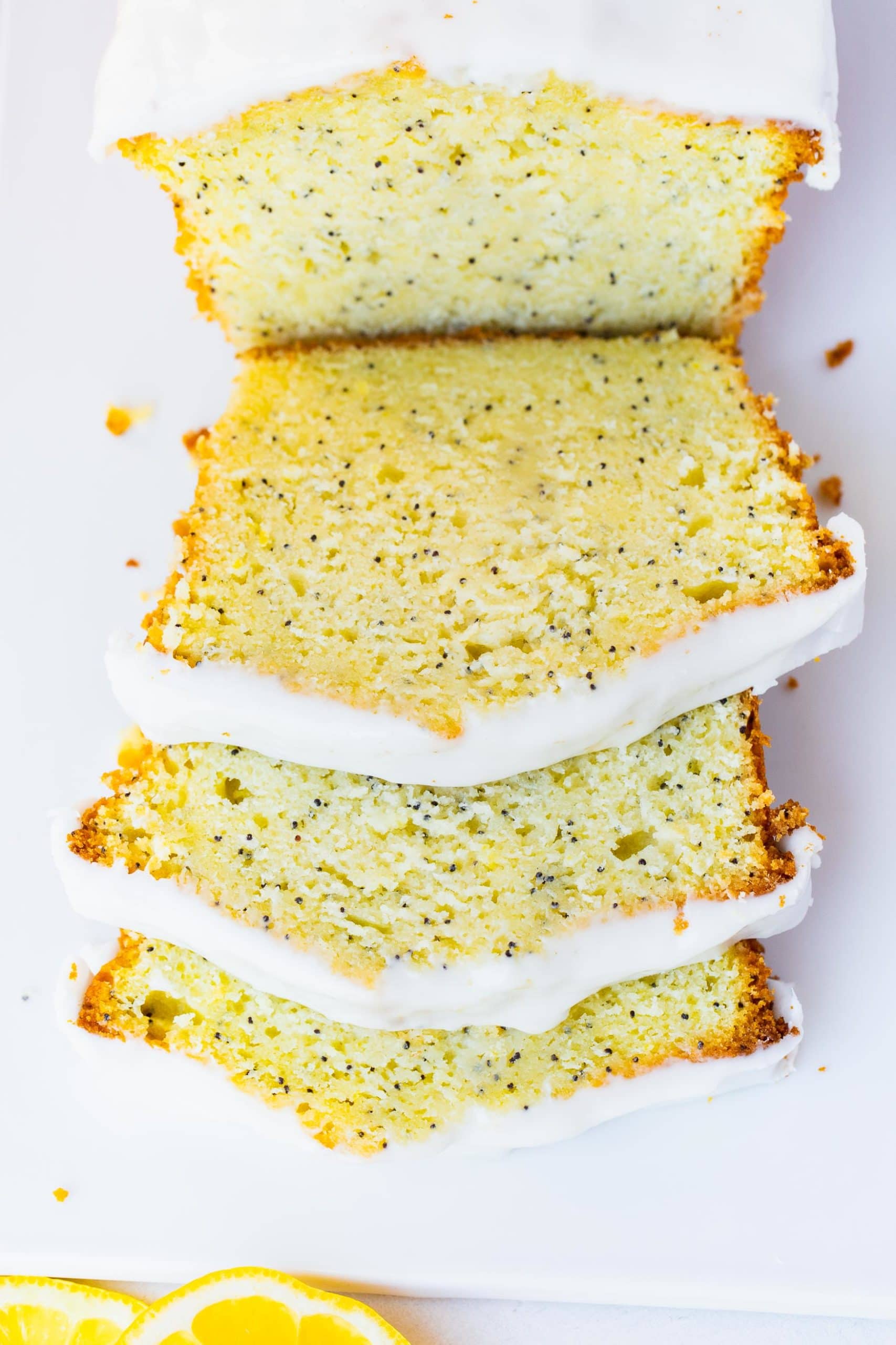 a photo of a lemon poppy seed loaf cake with three slices laying down staggered on top of each other.