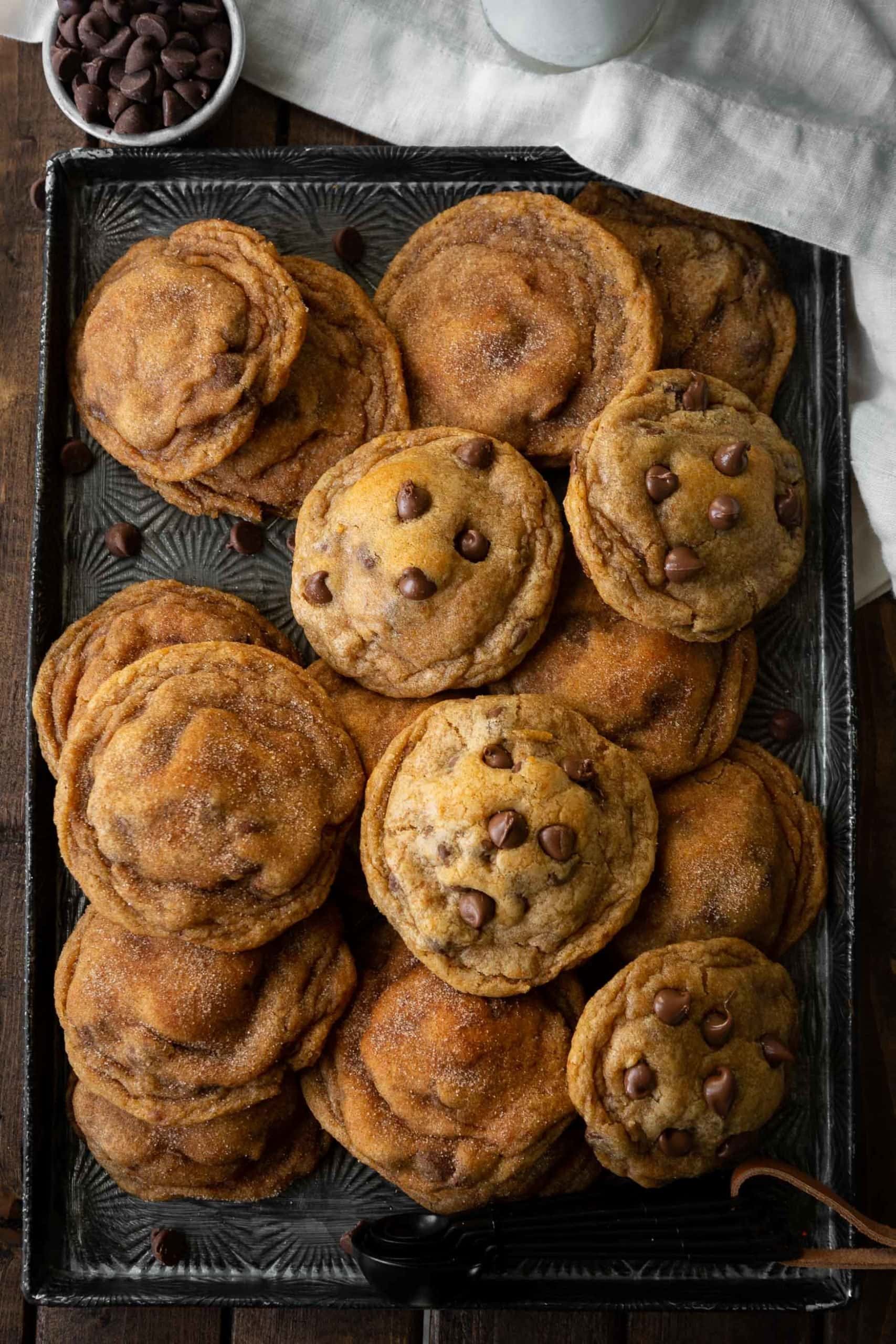 a photo of a cookie sheet full of baked pumpkin pudding cookies. some have chocolate chips and some are covered with cinnamon and sugar.