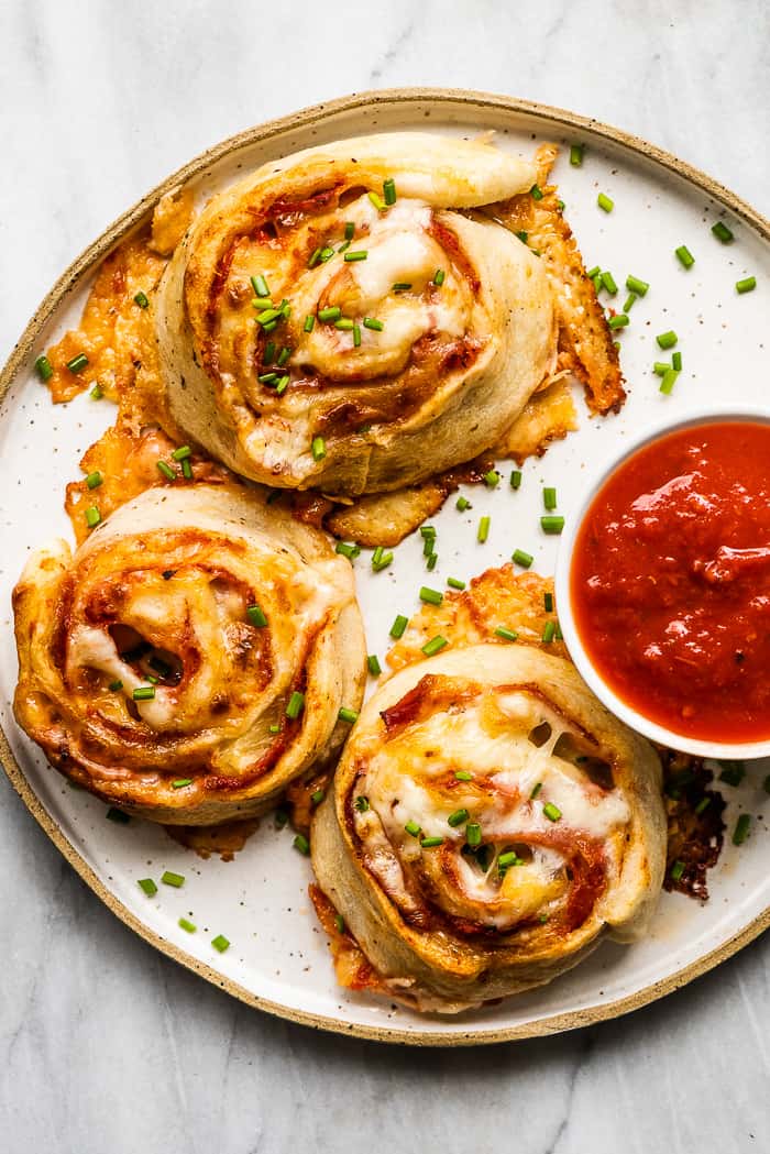 A white plate with pizza pinwheels and a red dipping sauce. A white plate with pizza pinwheels and a red dipping sauce.