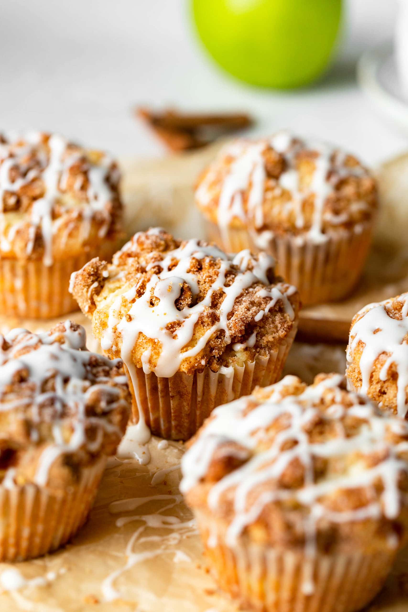 a bunch of apple coffee cake muffins with streusel and icing sitting on natural parchment paper