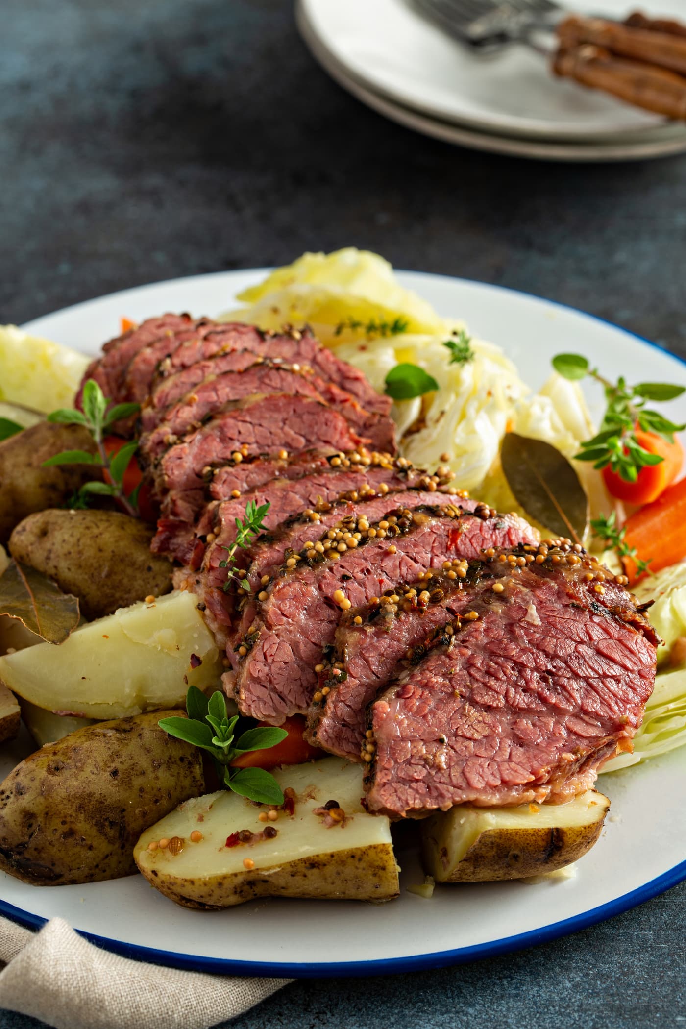 A serving tray with sliced corned beef surrounded by potatoes, carrots and cabbage with sprigs of herbs on top.