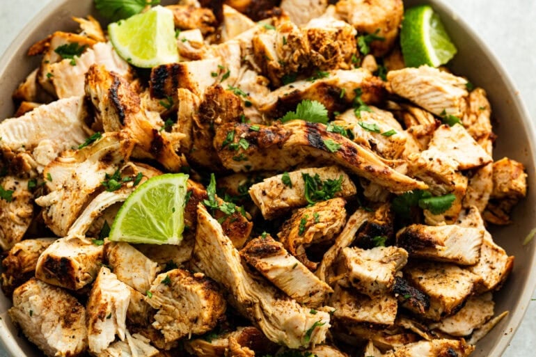 A close up photo of juicy Mexican Grilled Chicken shredded in a beige bowl with a squeeze of fresh lime juice on top.