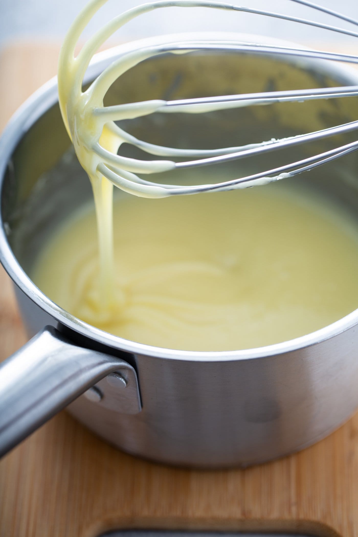 A pot with melted white chocolate. A whisk with white chocolate dripping from the end is held above the pot.