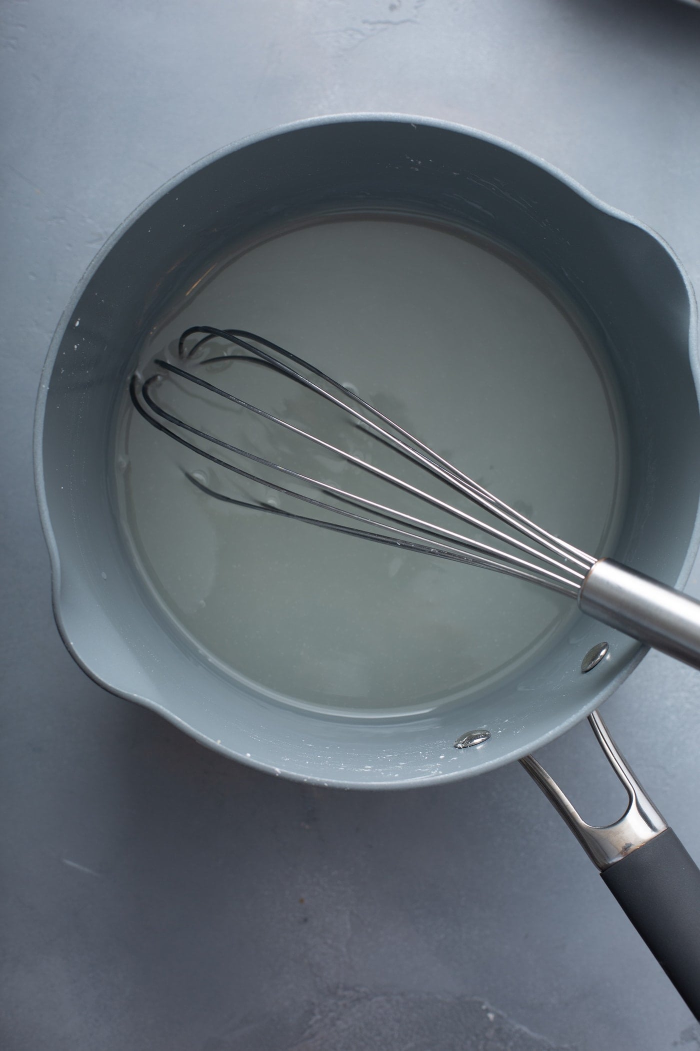 A saucepan with water and sugar and a whisk.