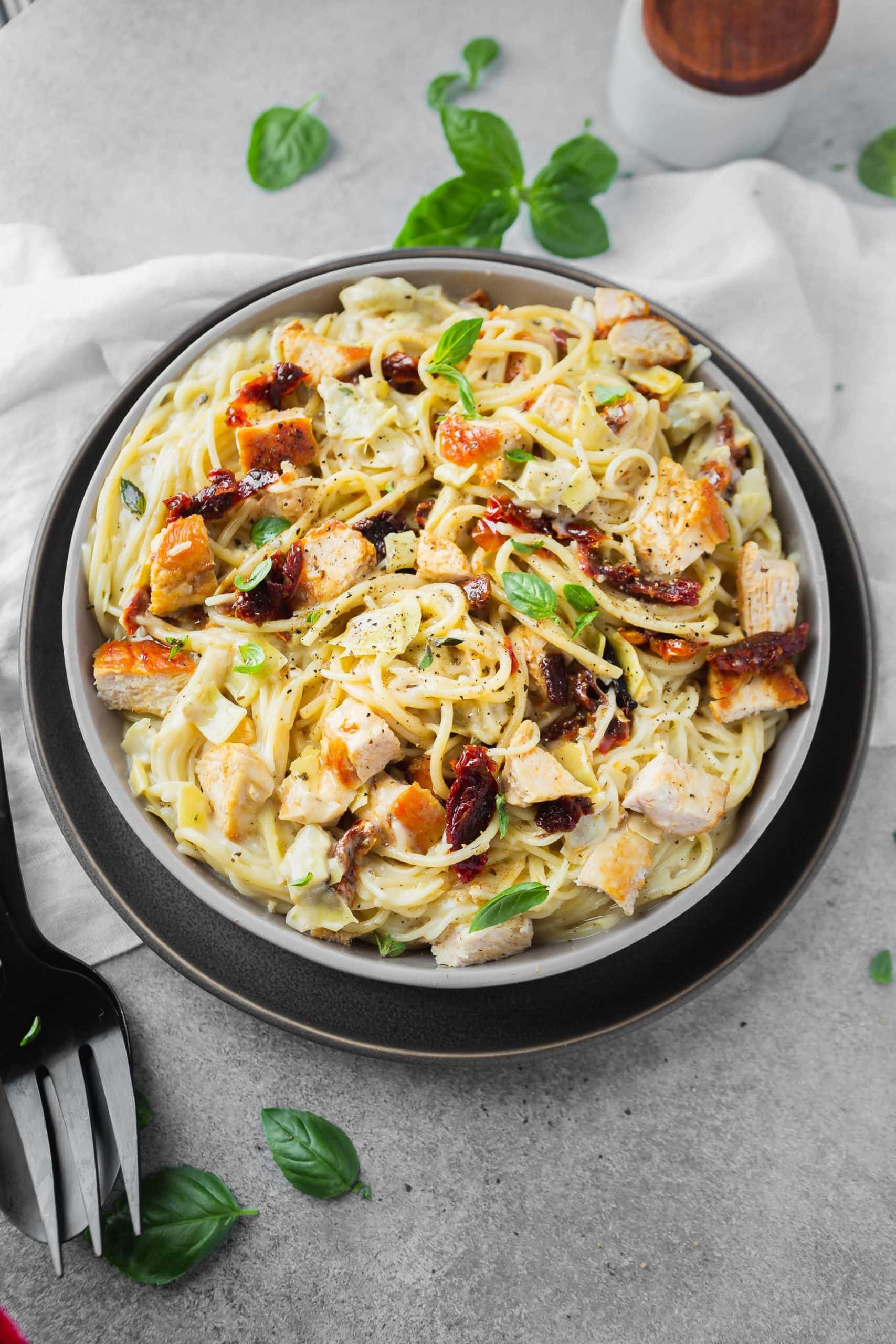 a photo of creamy chicken pasta with sun dried tomatoes and fresh basil on top.