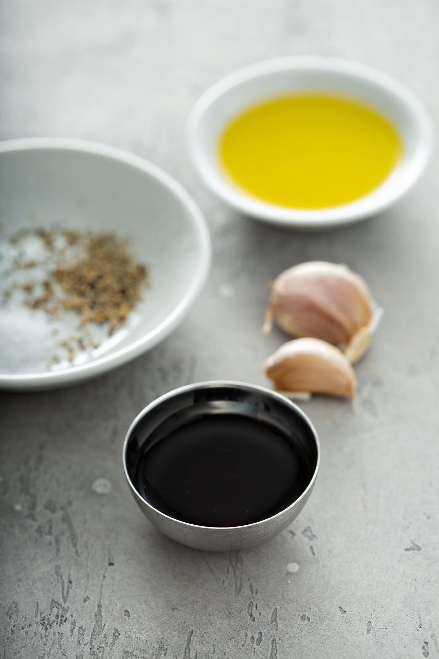 Small containers of spices, balsamic vinegar, oil and two cloves of garlic.