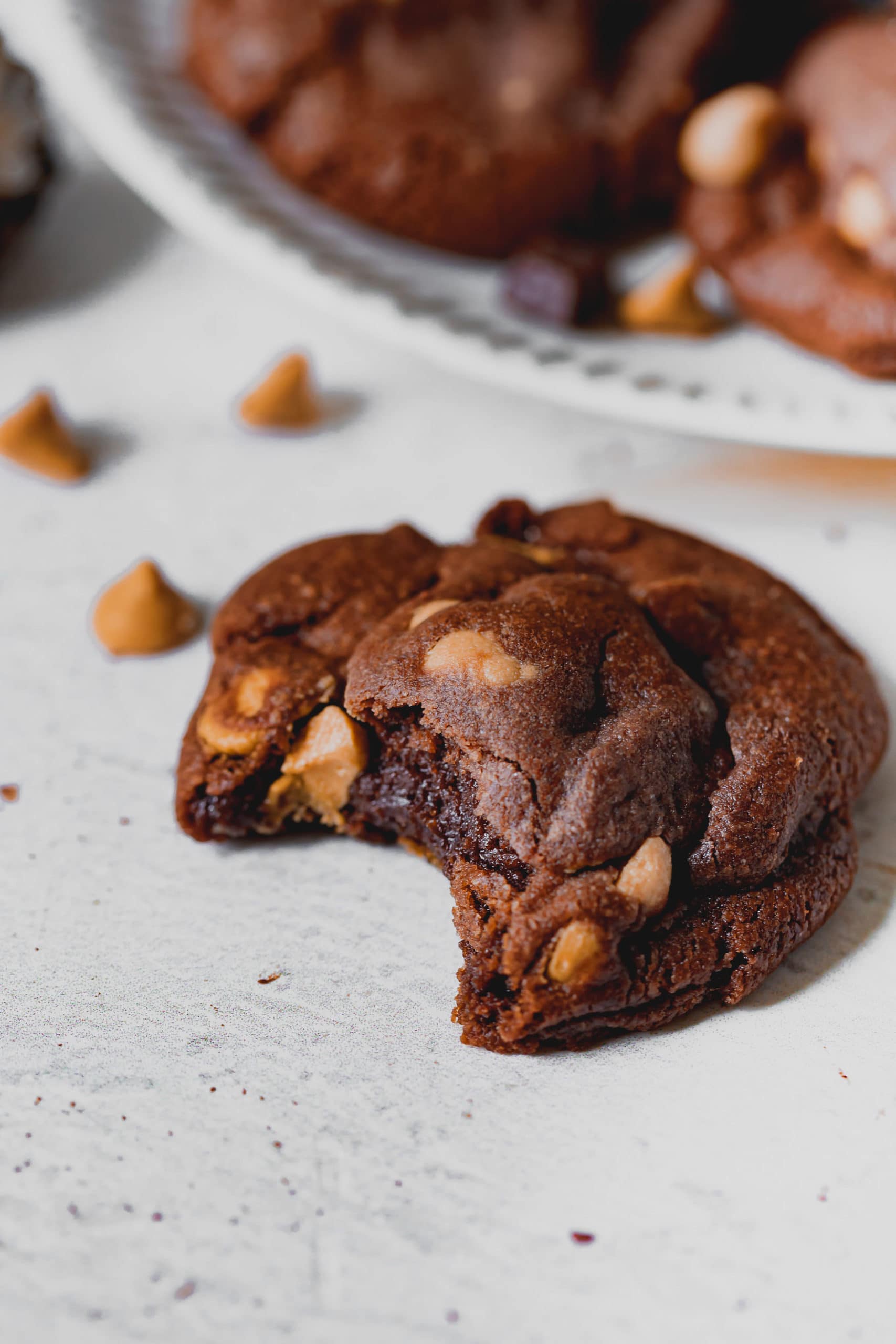 A peanut butter chocolate cookie that is broken in half. The chocolate cookie has peanut butter chips in it.