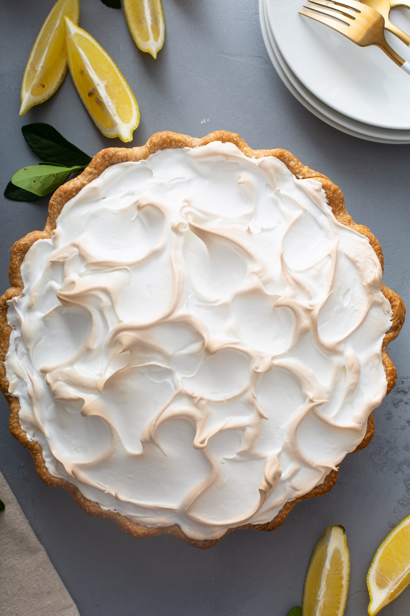 A top view of a lemon meringue pie with fluffy toasted meringue on top. There are a few lemon wedges next to the pie.