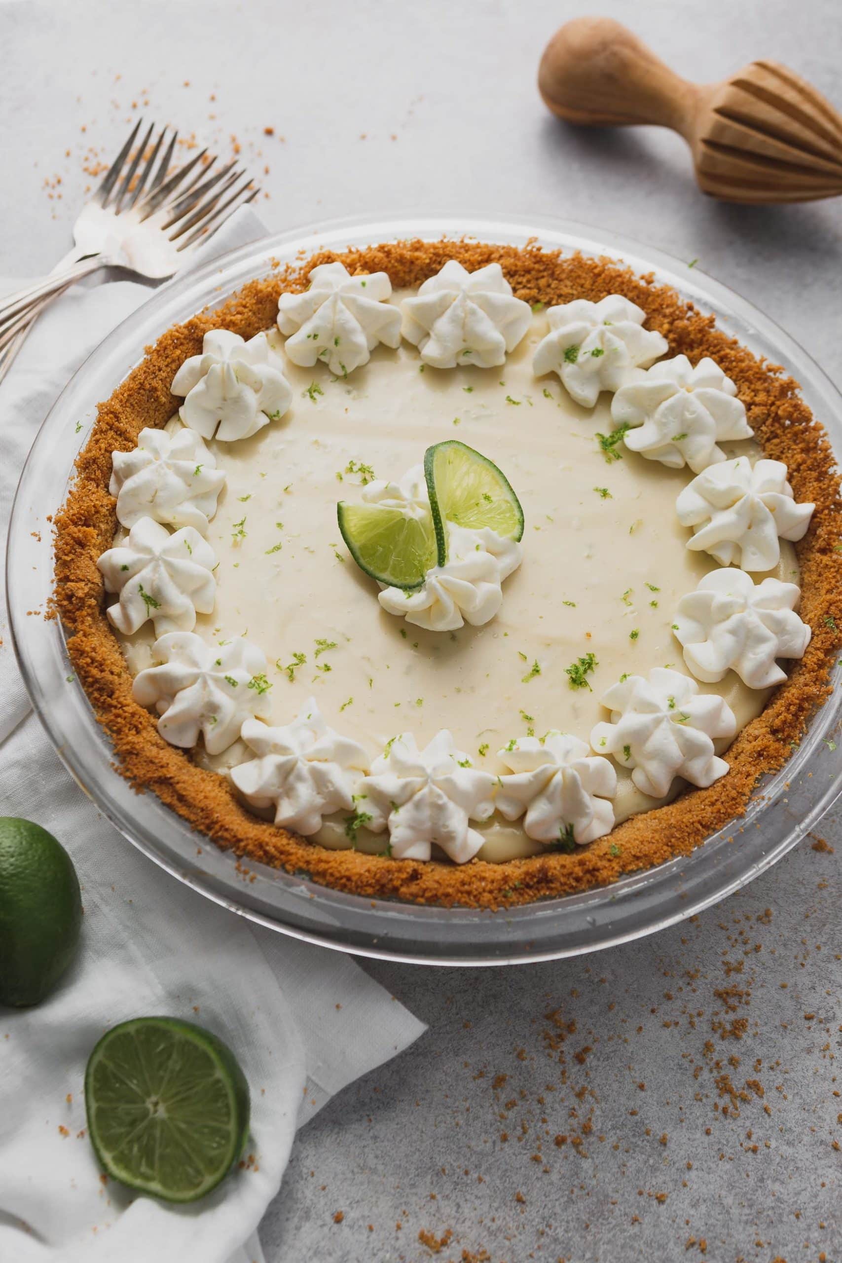 A key lime pie in a graham cracker crust. The top is decorated with whipped cream and slices of lime.