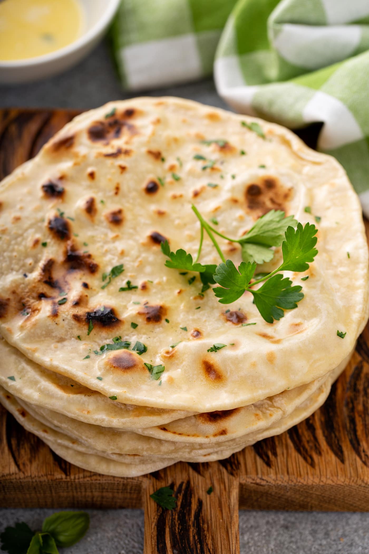 A photo of a stack of cooked discs of unleavened bread topped with chopped fresh parsley and a sprig of fresh parsley.