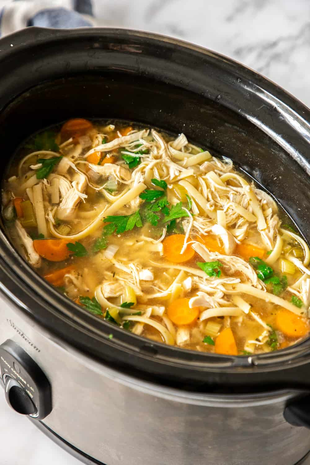 chicken noodle soup in the black bowl of a slow cooker