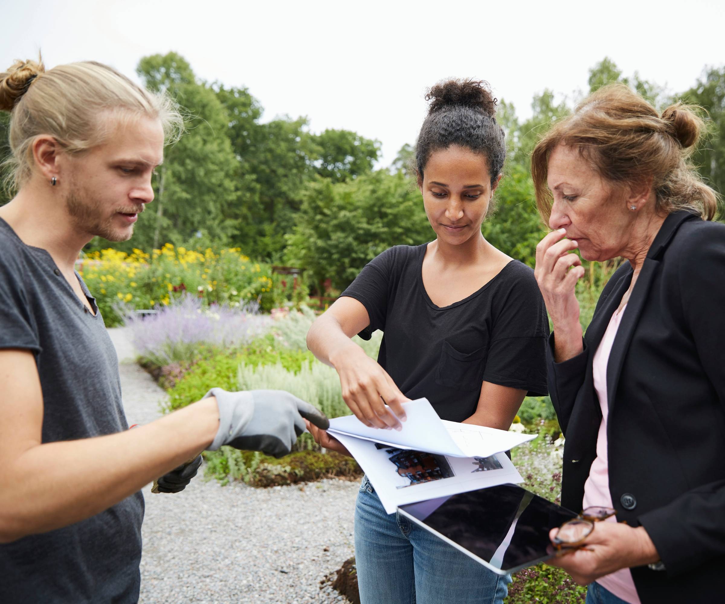 A man and two women talking over papers in a garden