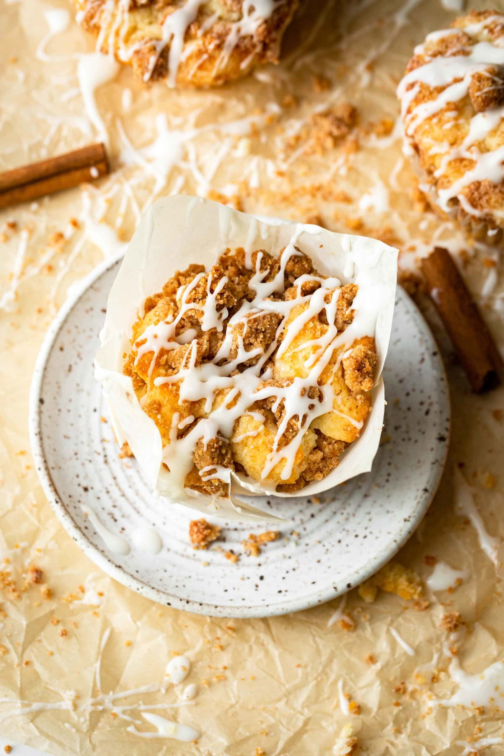 a photo of a single of coffee cake muffin in a white tupli liner on a small dessert plate topped with streusel and an icing drizzle.