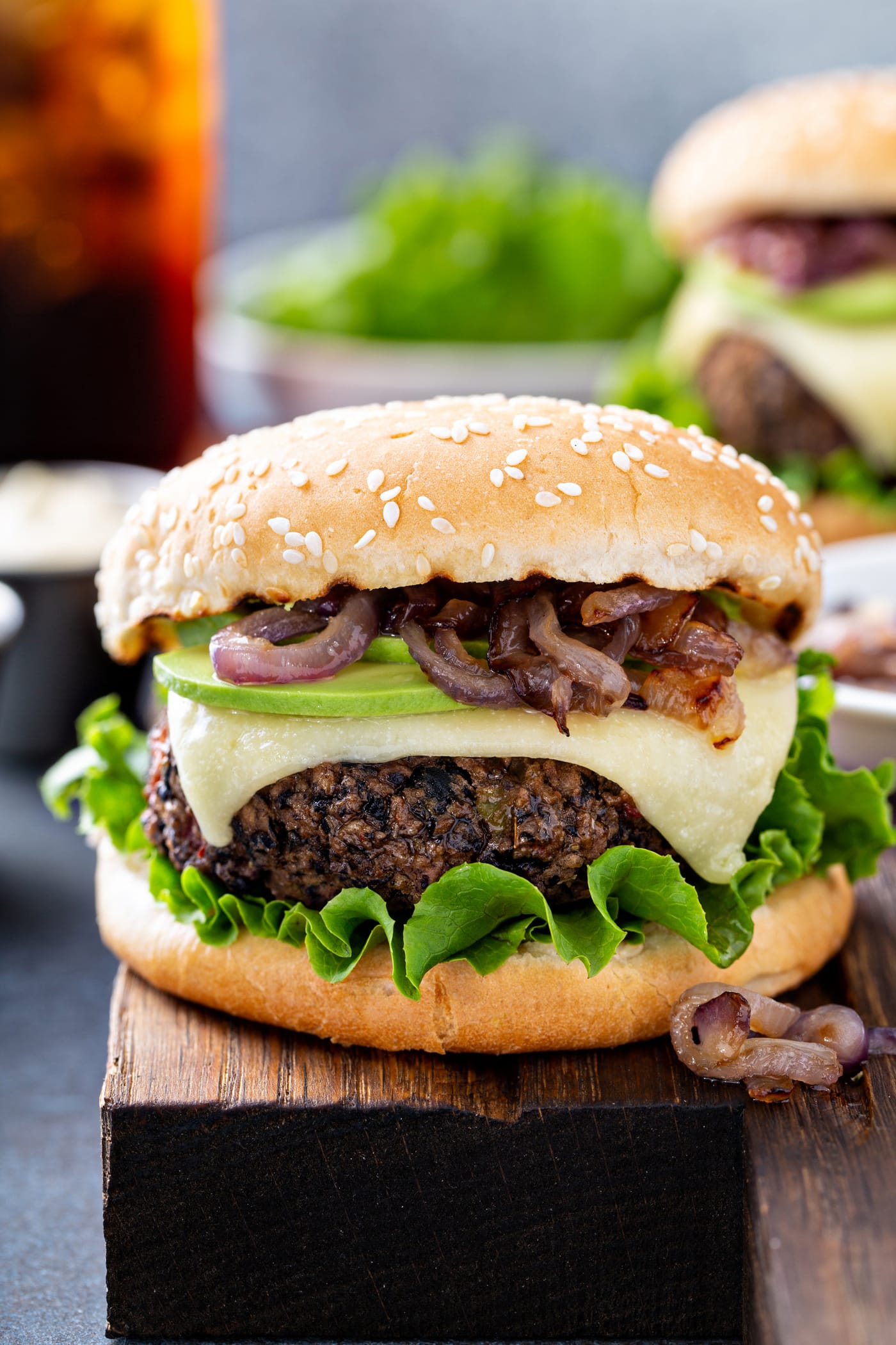 A black bean burger on a sesame seed bun. It is dressed with onions, cheese and lettuce.