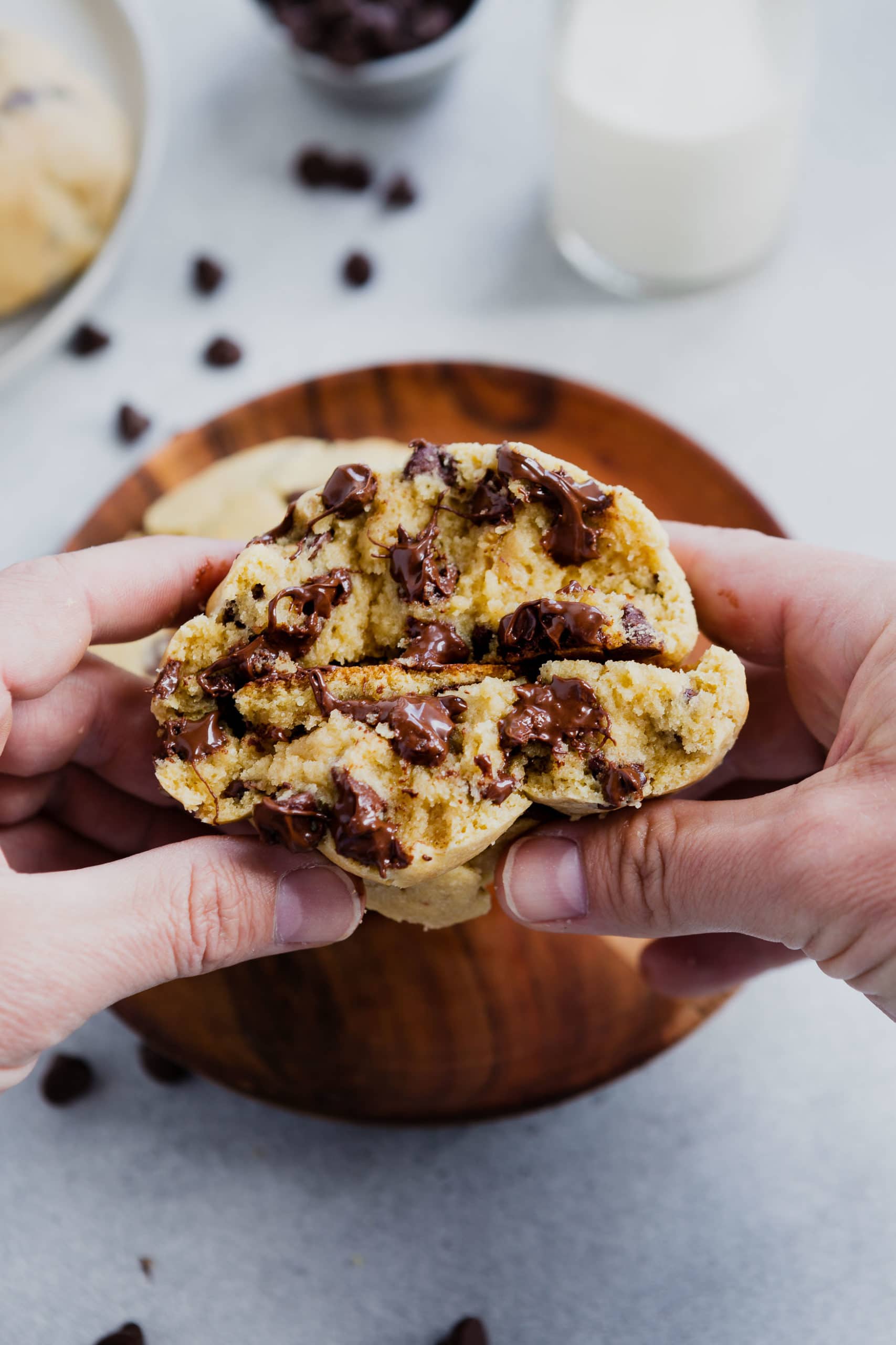a photo of someone holding a thick chocolate chip cookie that has been broken in half with the bottoms of each side touching eatch other.