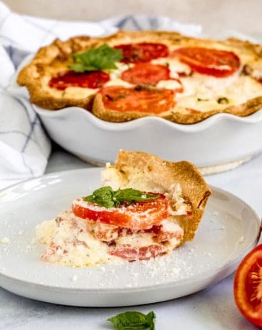 Alabama Tomato Pie slice on white plate with pie dish behind it.