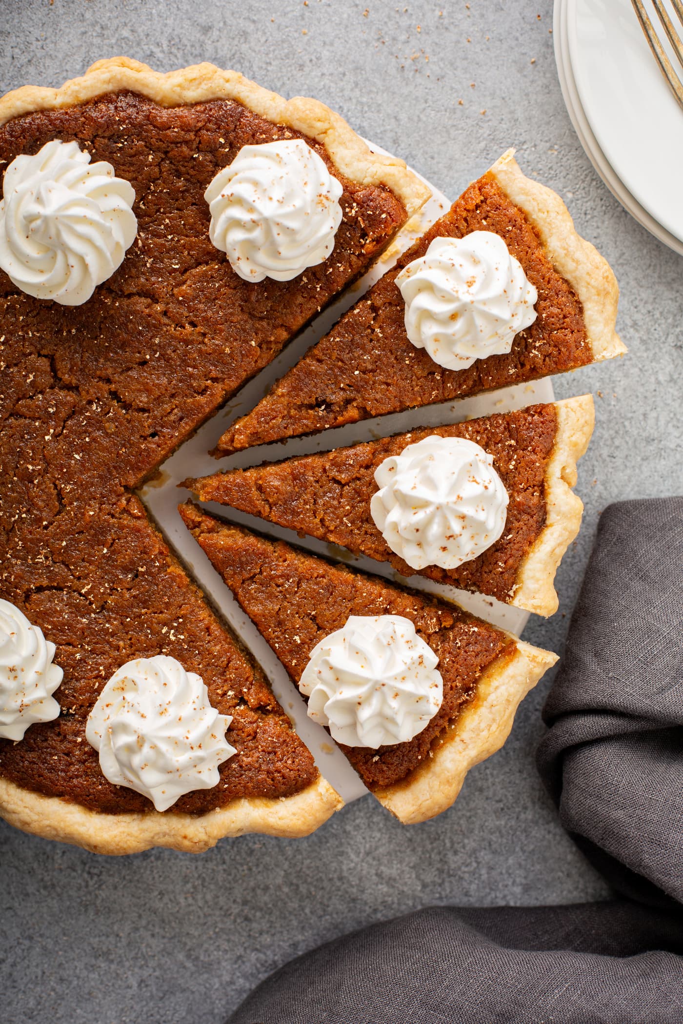 A photo of a whole sweet potato pie with dollops of whipped cream on top and three slices pulled out from the whole pie.
