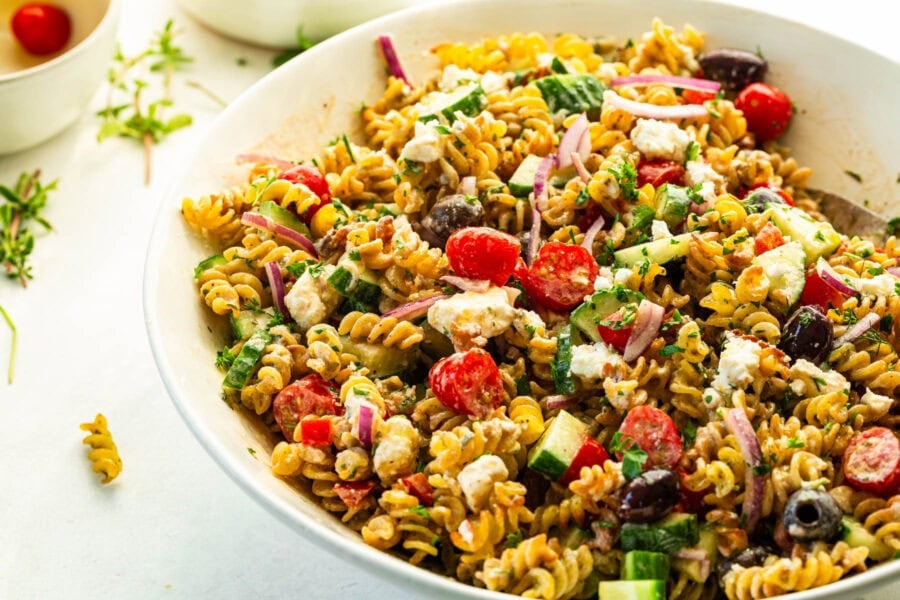 a large white serving bowl of crispy Greek pasta salad with feta, kalamata olives, tomatoes and a creamy dressing