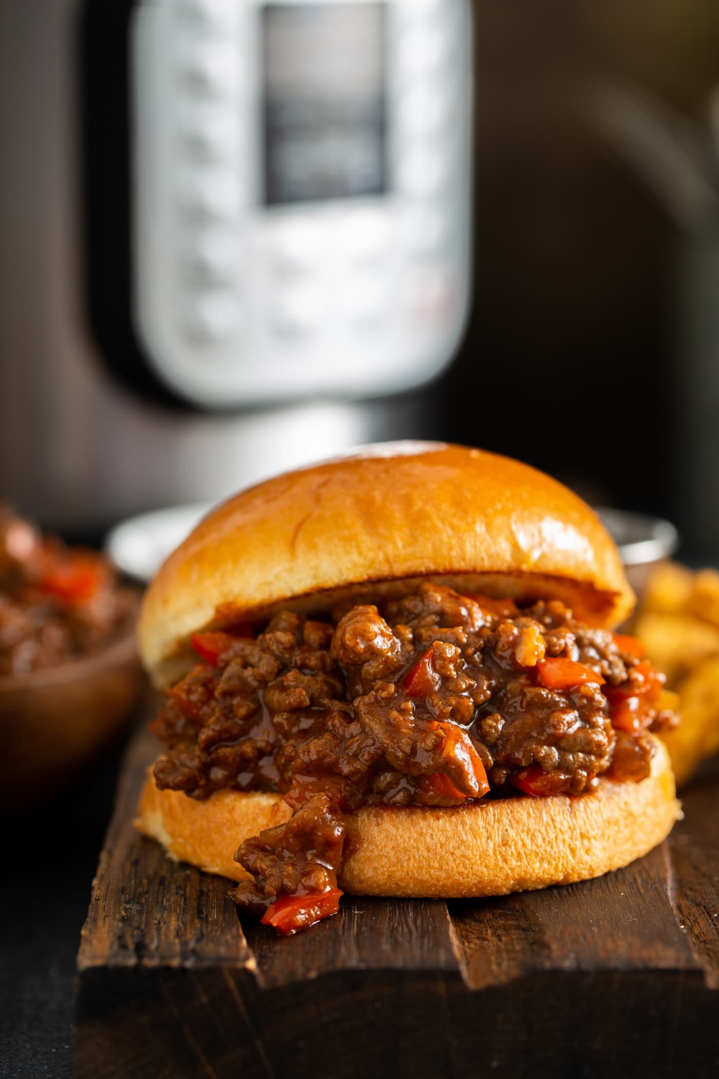Sloppy joe on a toasted bun. The sloppy joe filling has browned ground beef and chopped red bell peppers in a thick sauce. There is an instant pot sitting behind the sloppy joe.