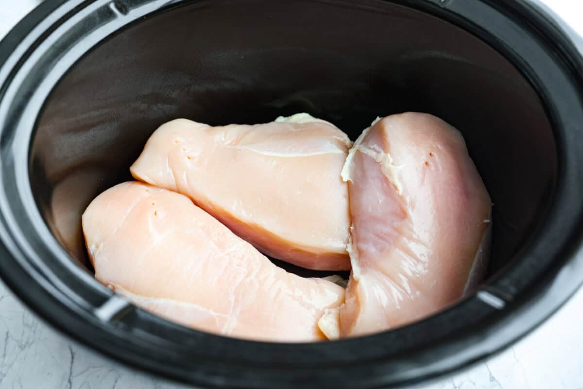 Slow cooker with chicken breasts added. 