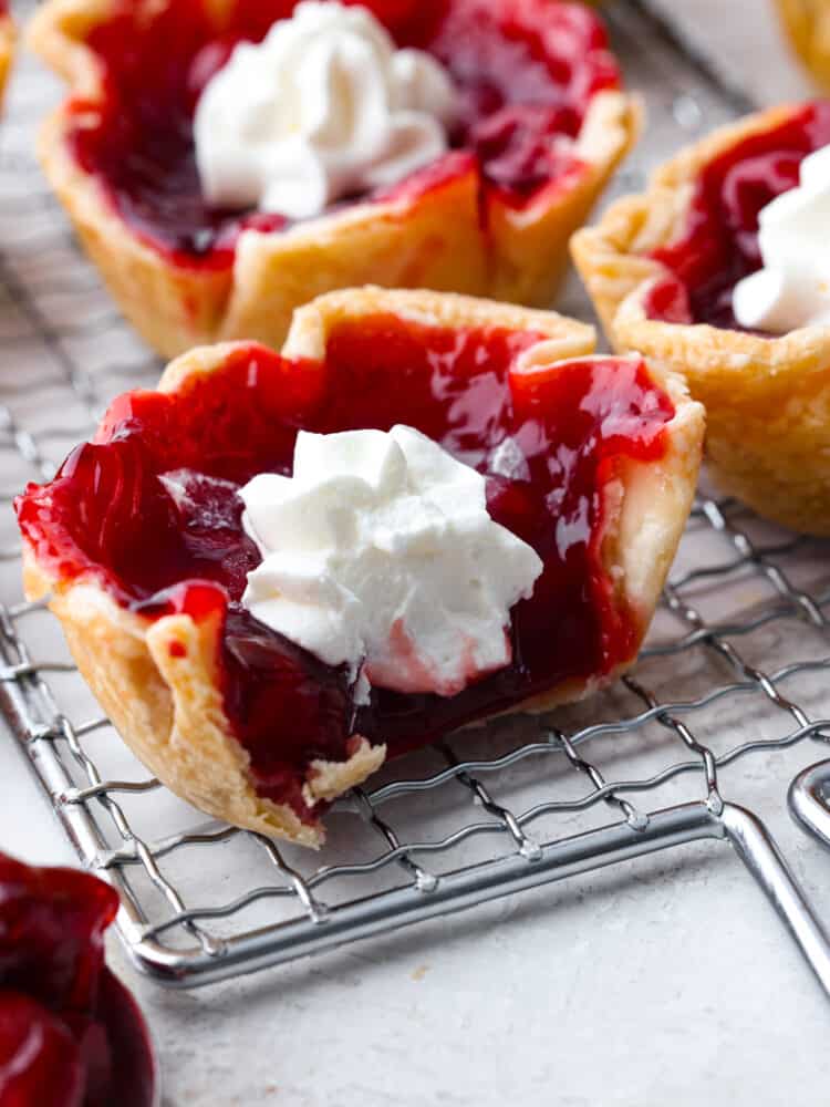A mini cherry pie on a cooling rack that has a bite taken out of it. 