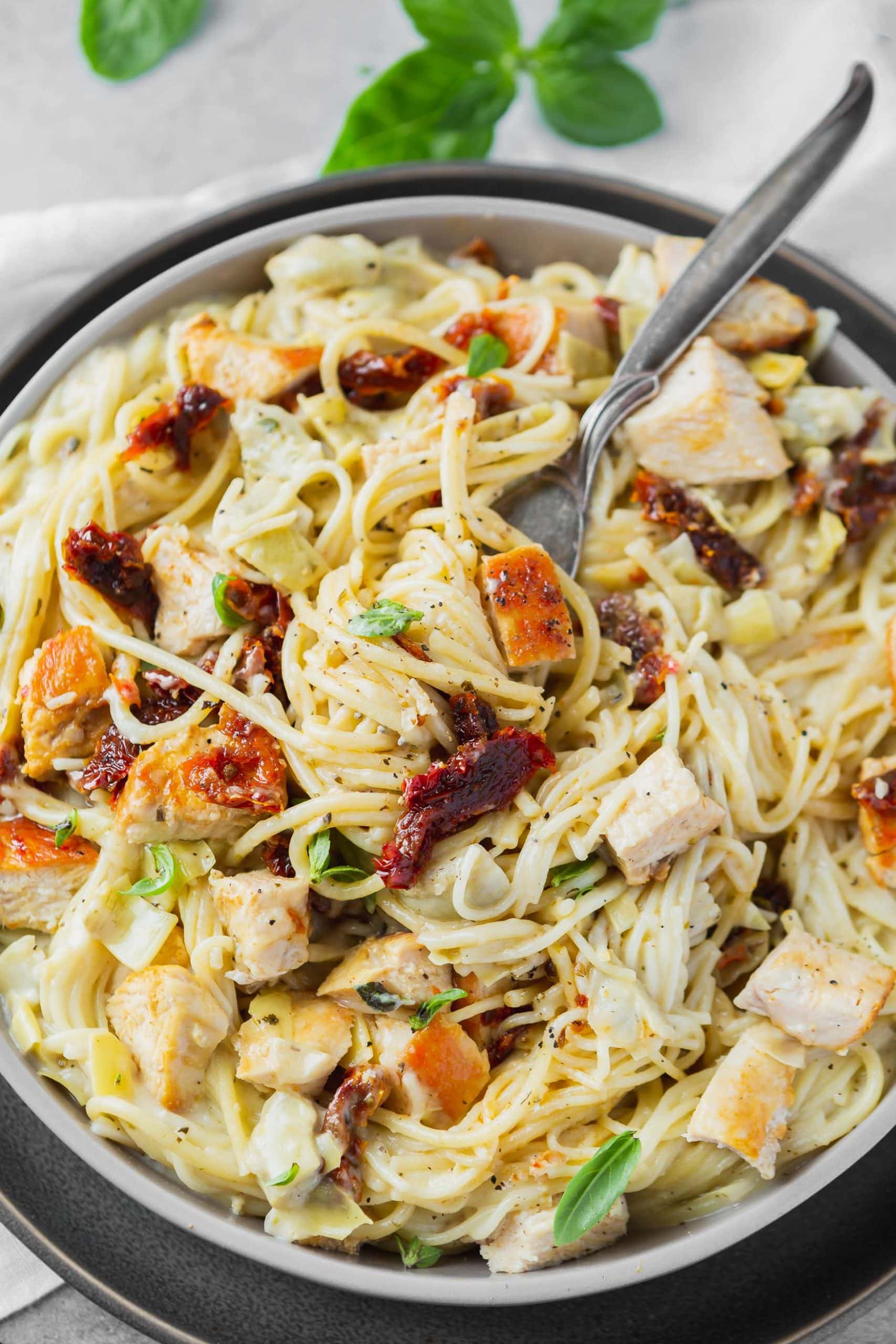 a photo of creamy chicken artichoke pasta with a fork twirling up a bite.