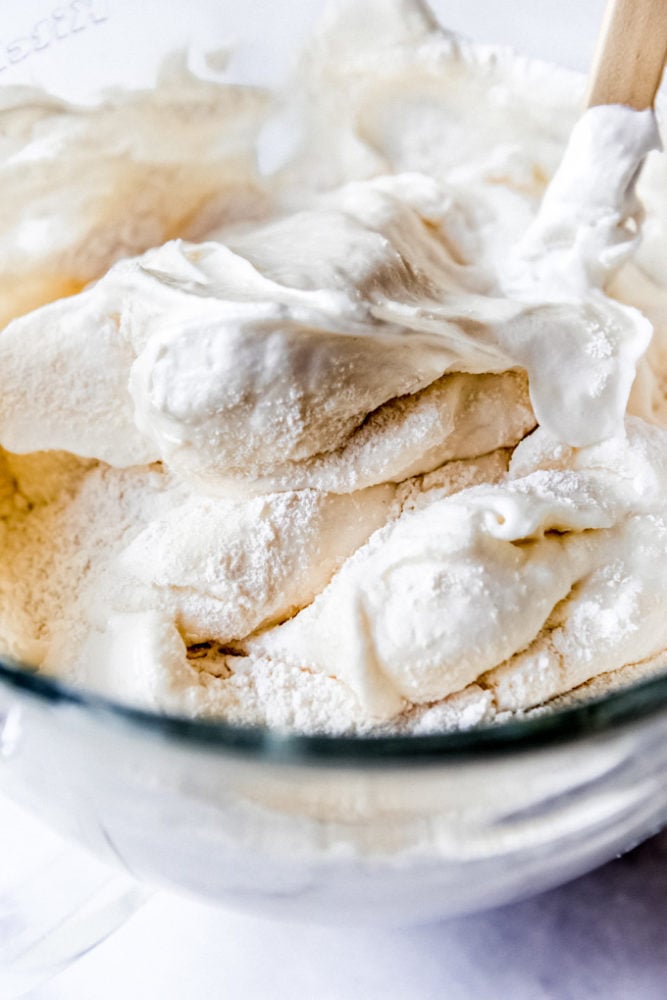Folding sifted flour and sugar into egg whites that have been whipped into soft peaks.