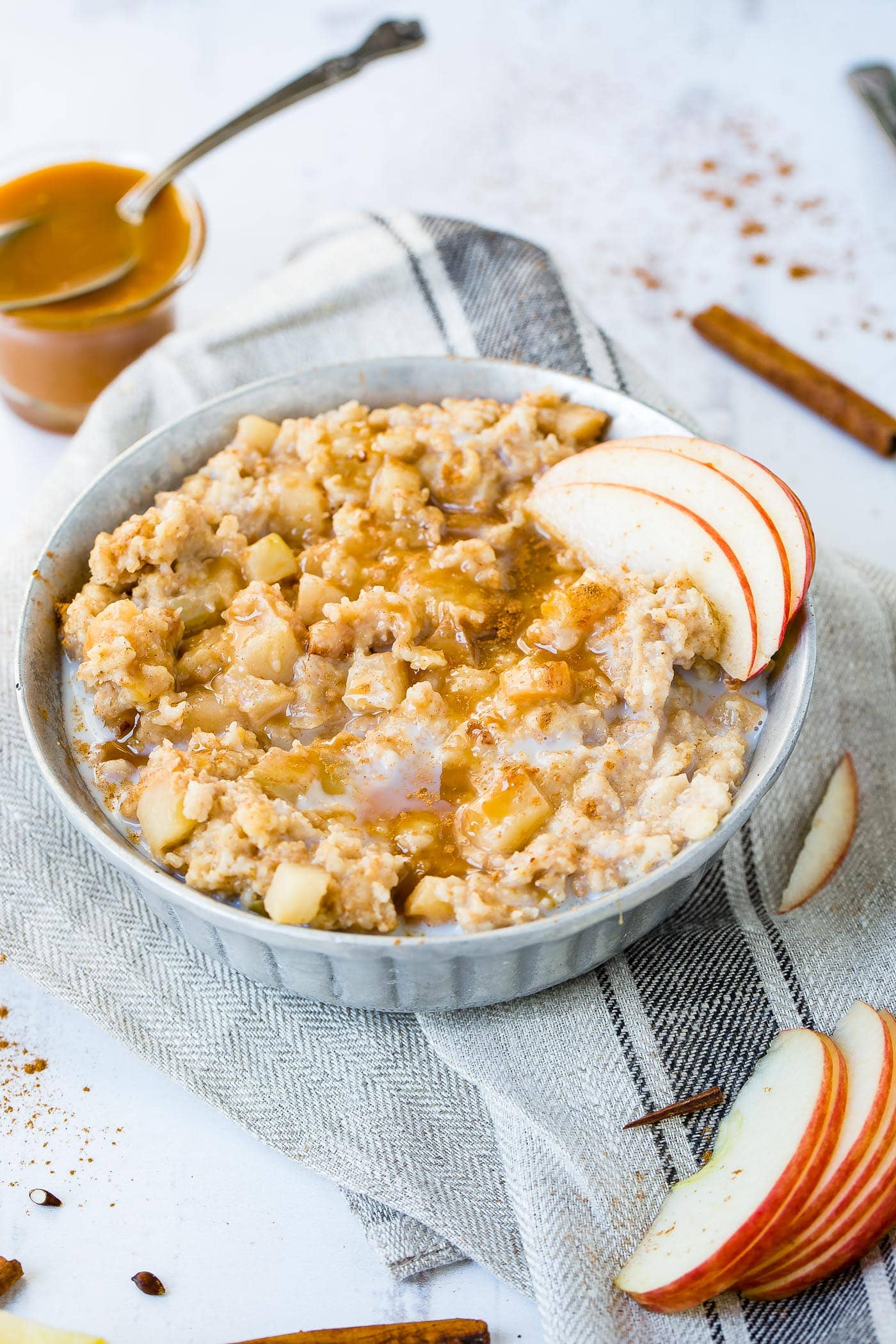 A photo of a bowl of oatmeal full of apple chunks and topped with caramel and thin apple slices.