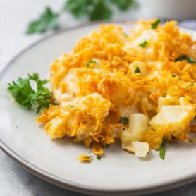 a photo of a serving of cheesy potato casserole on a white plate with golden crunchy topping.