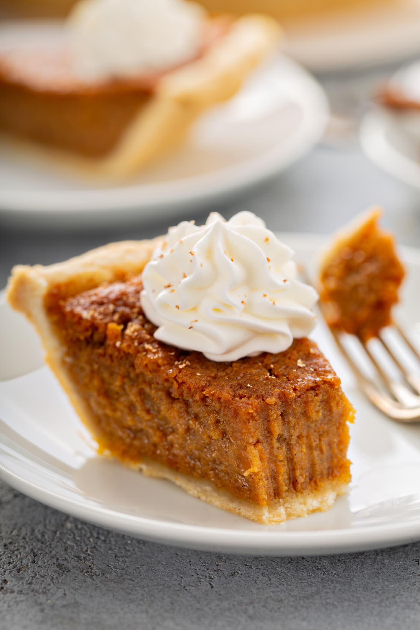 A photo of a bite of sweet potato pie being removed from a slice with a fork.