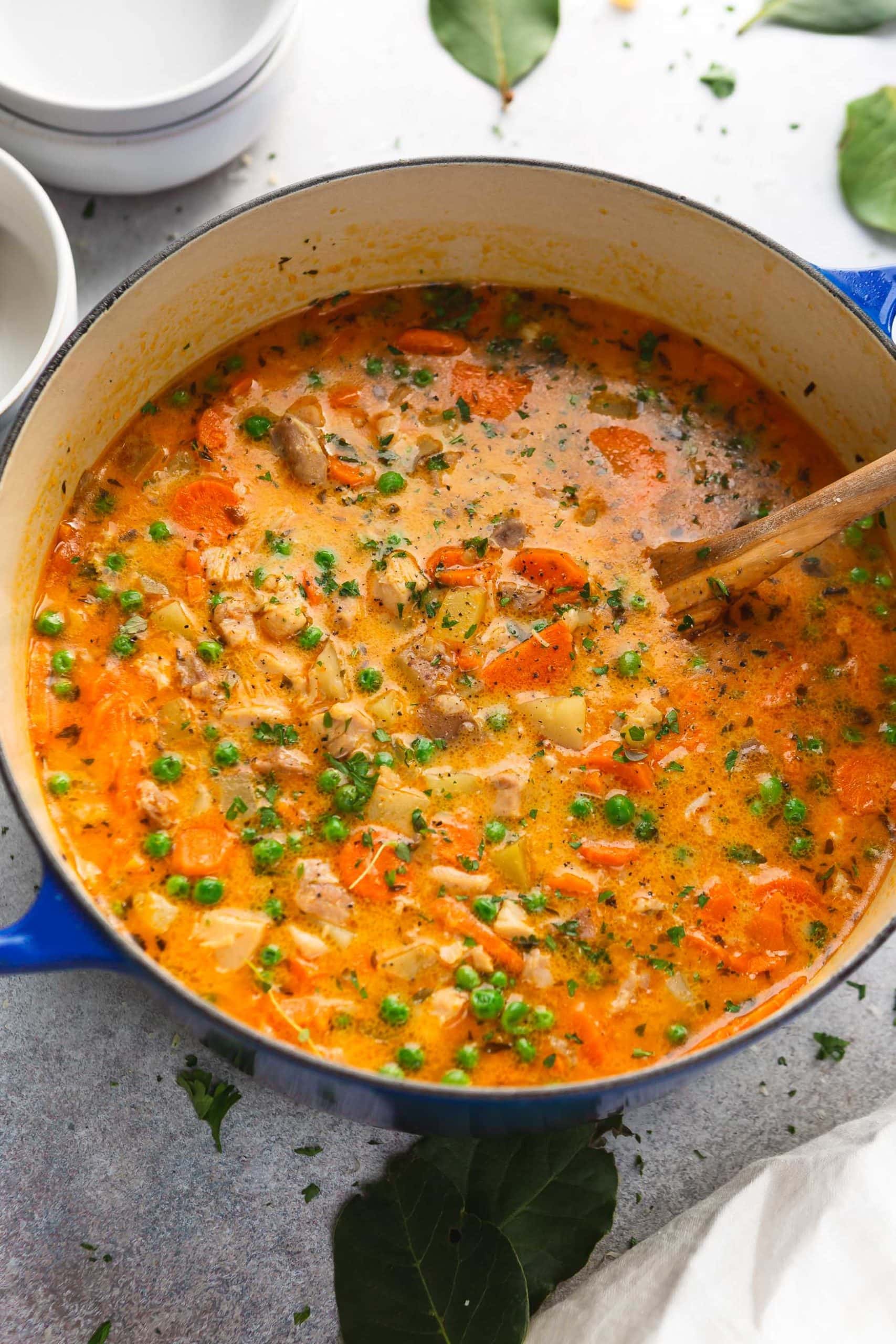 A pot of thick slow cooker chicken stew with a wooden spoon in it. The stew is packed with bright vegetables, chicken and herbs.