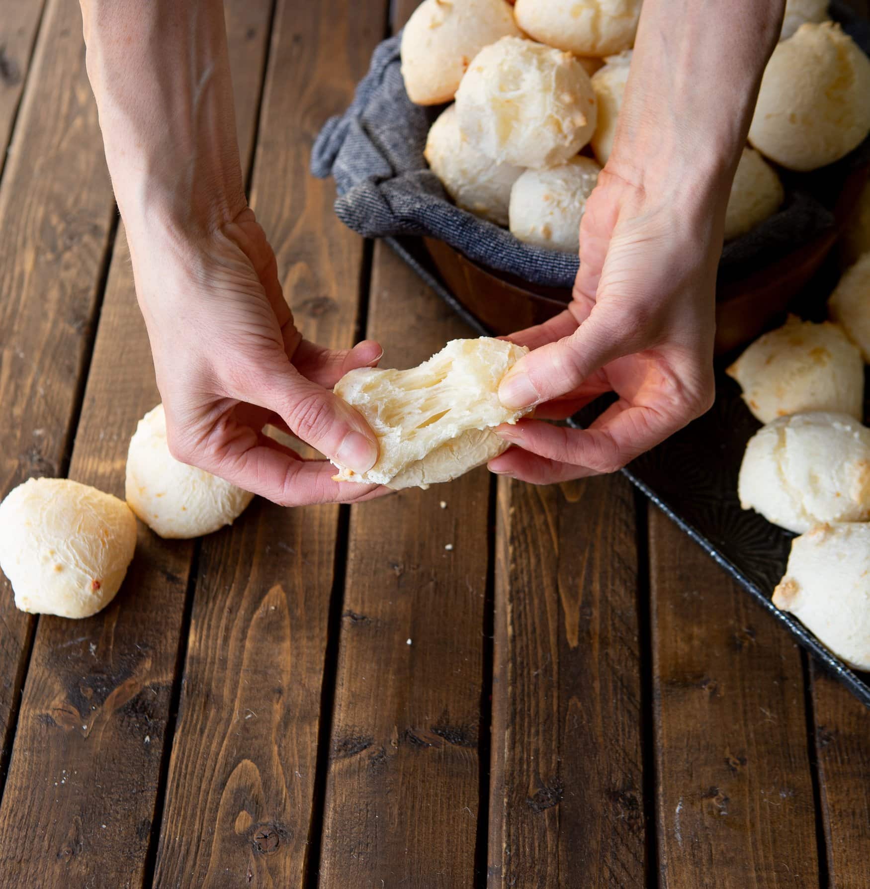 a photo of someone pulling apart one piece of pao de queijo to show the cheesy center.