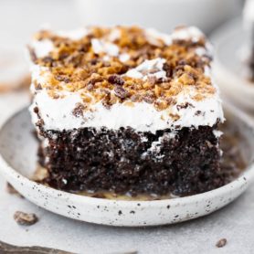 a photo of a single piece of chocolate cake topped with whipped cream and toffee bits and the cake is oozing caramel on the saucer it is sitting on.