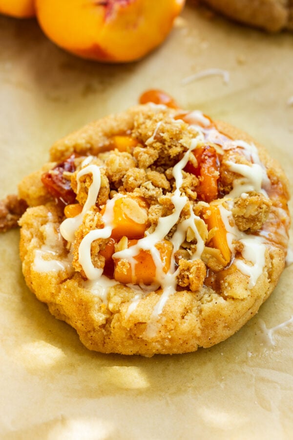 a photo of a golden baked cinnamon sugar cookie base filled with juicy peach filling and topped with a crunchy oat topping and a vanilla drizzle