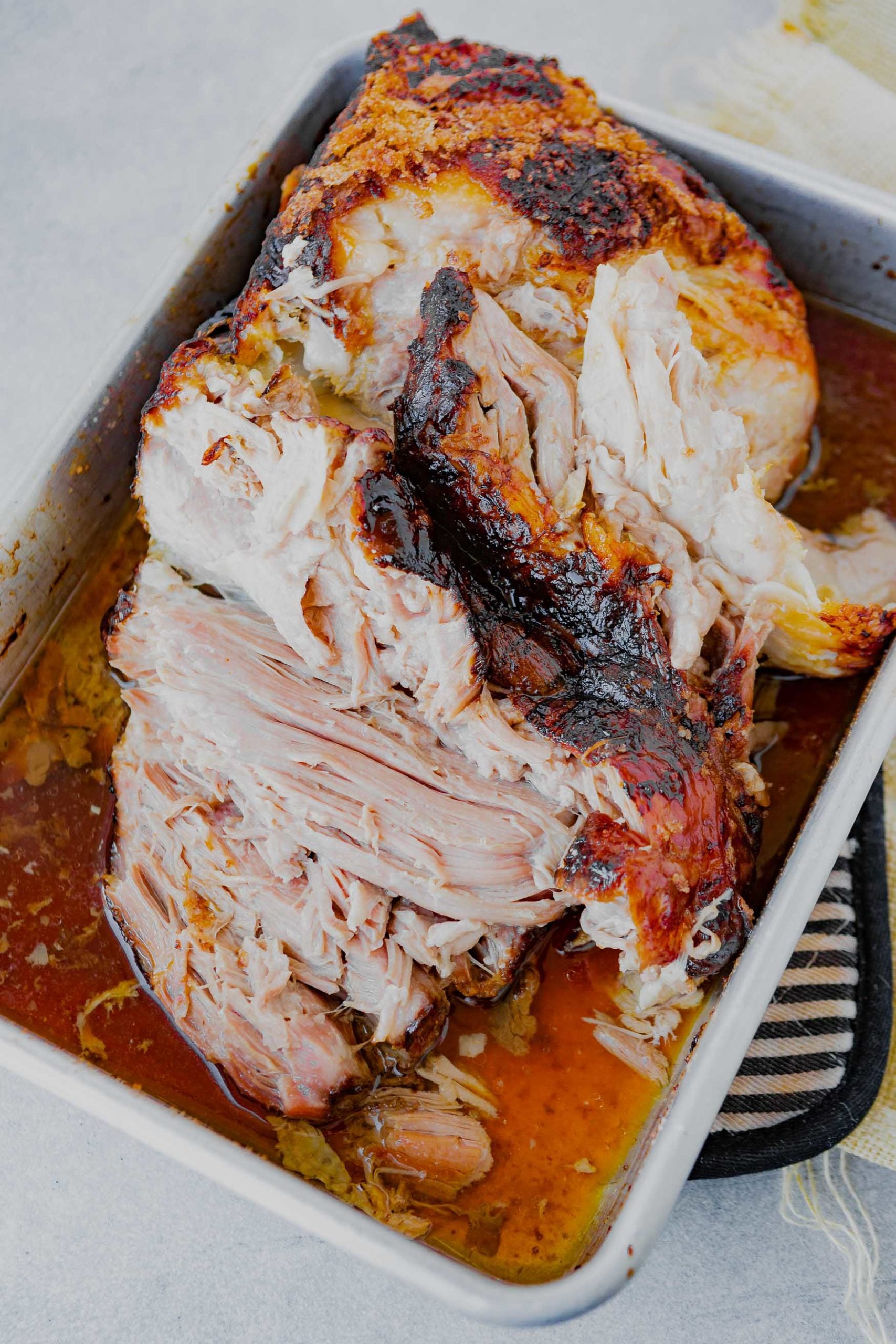 a photo of a tender pork roast starting to be shredded in a white baking dish. 