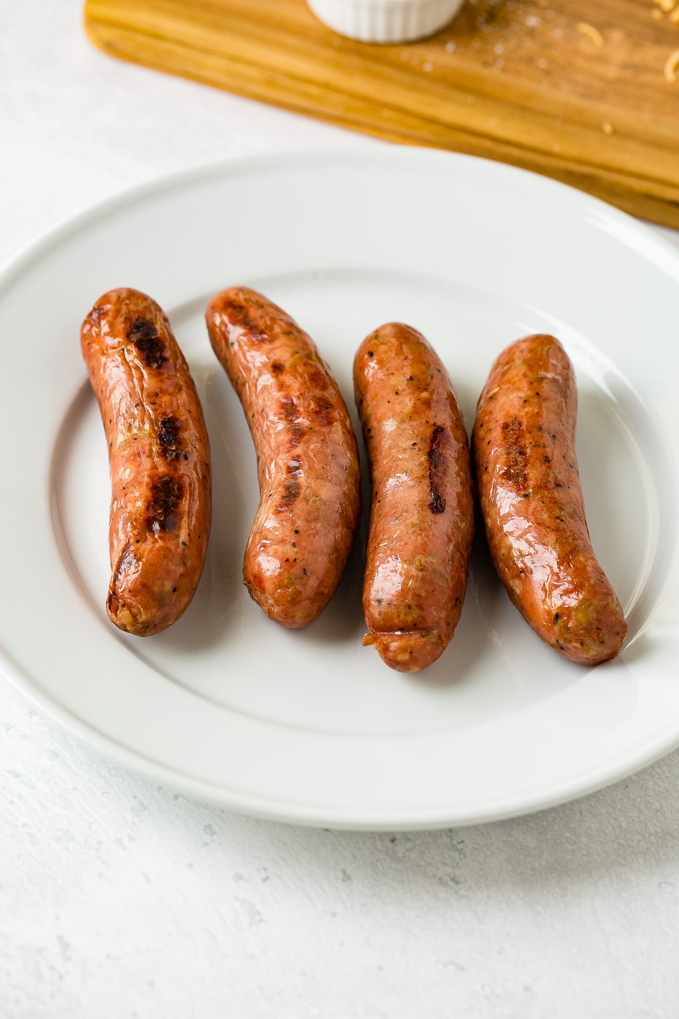 Four apple chicken sausages on a white plate.
