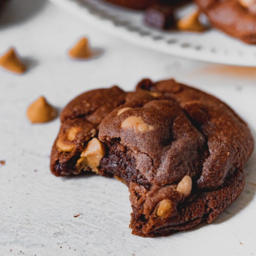 A peanut butter chocolate cookie that is broken in half. The chocolate cookie has peanut butter chips in it.